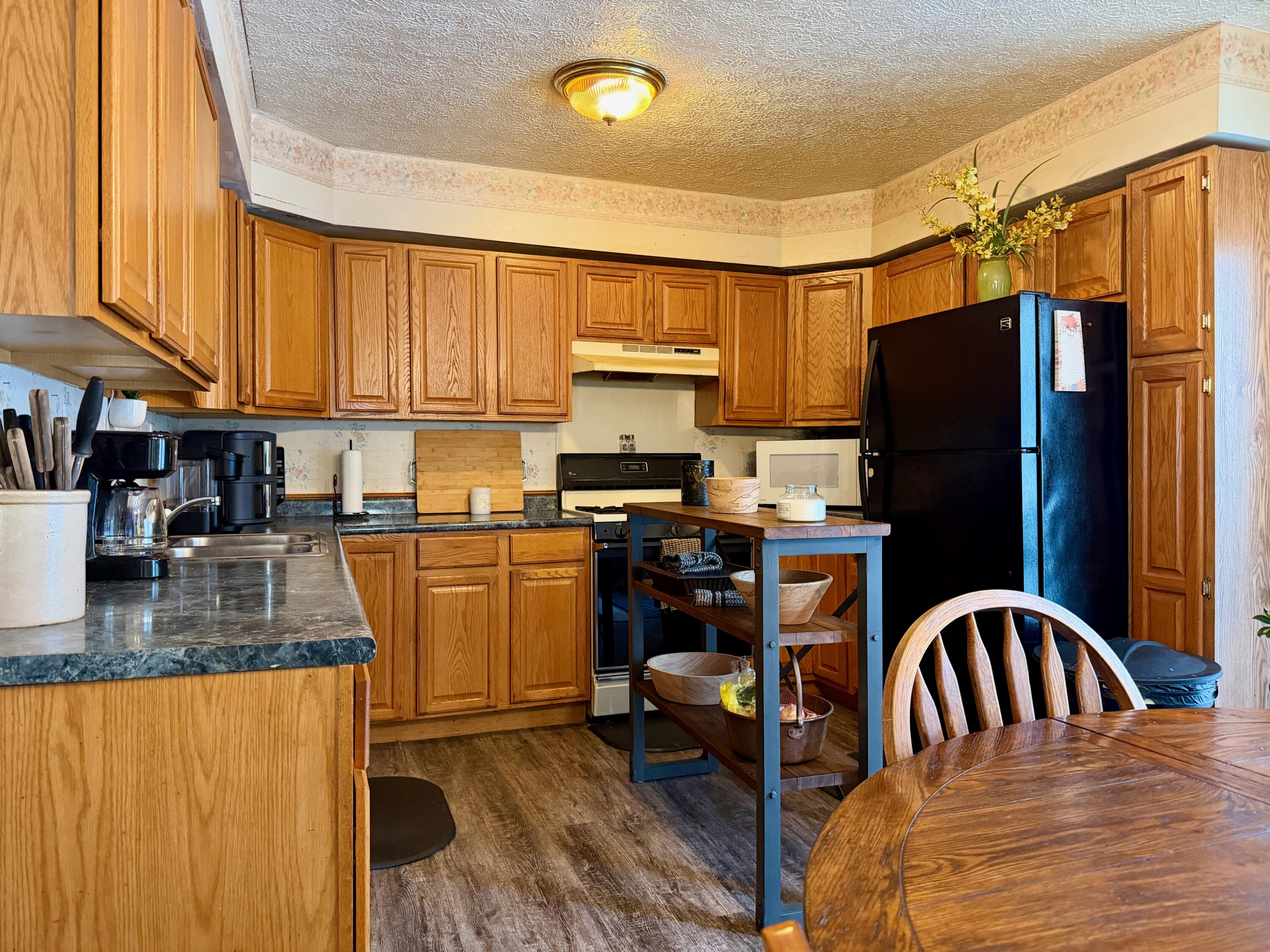 109 South Jefferson Street Hamlet, IN 46532 - Photo 5 of 14 a kitchen with granite countertop a refrigerator a stove a sink a dining table and chairs with wooden floor