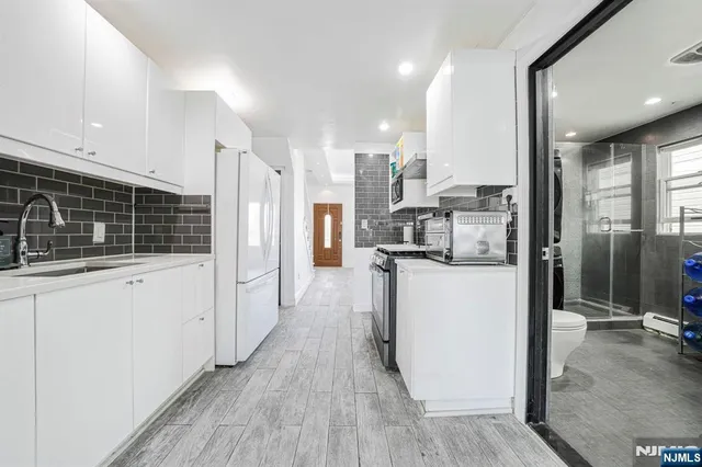 a kitchen with stainless steel appliances kitchen island granite countertop a refrigerator a stove a oven and white cabinets with wooden floor