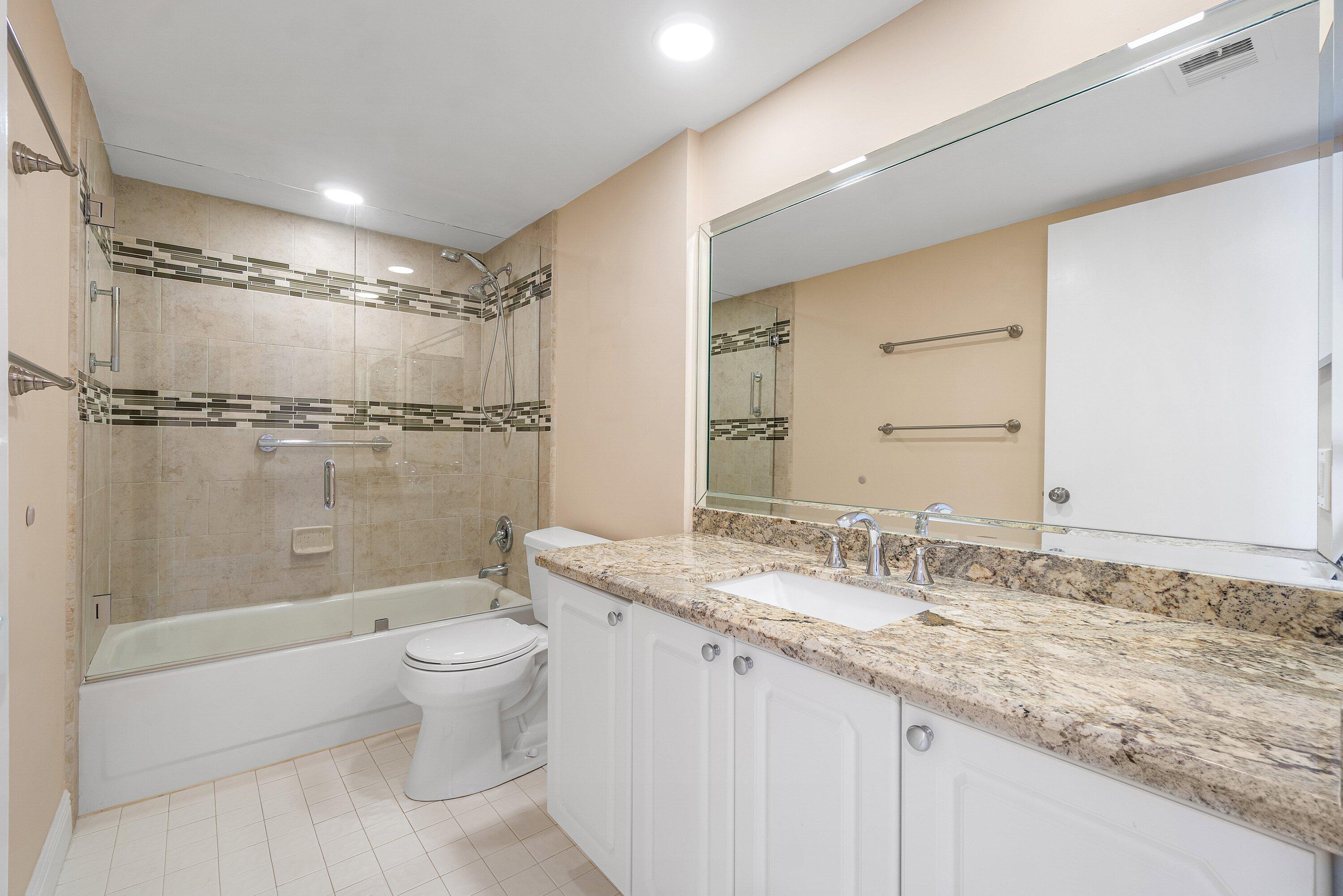 14096 Huntington Pointe Drive, Unit 106 Delray Beach, FL 33484 - Photo 26 of 47 a bathroom with a granite countertop sink a toilet a mirror and shower