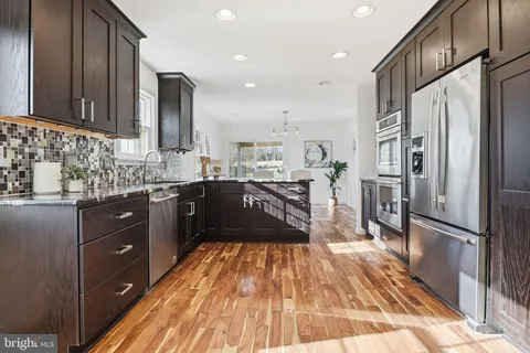 a kitchen with stainless steel appliances granite countertop a refrigerator a sink dishwasher a stove and white countertops with wooden floor