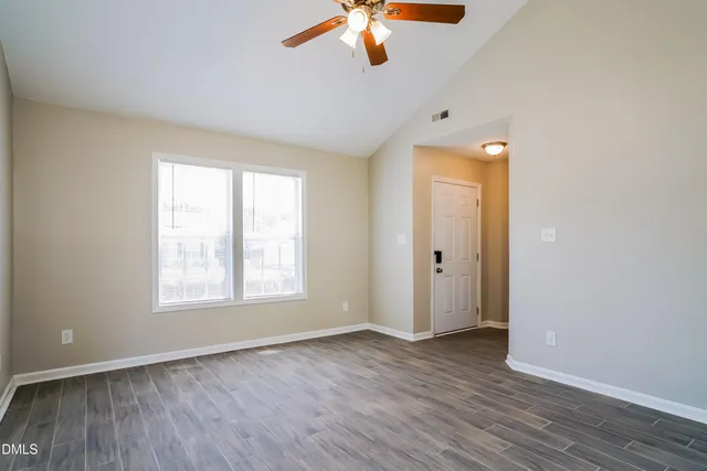 an empty room with wooden floor fan and windows