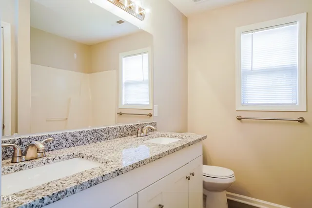 a bathroom with a granite countertop sink a toilet and a window