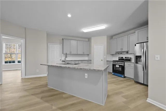 a kitchen with granite countertop a refrigerator oven a sink dishwasher and white cabinets with wooden floor