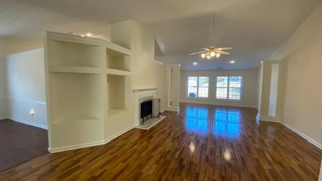an empty room with wooden floor fan and windows