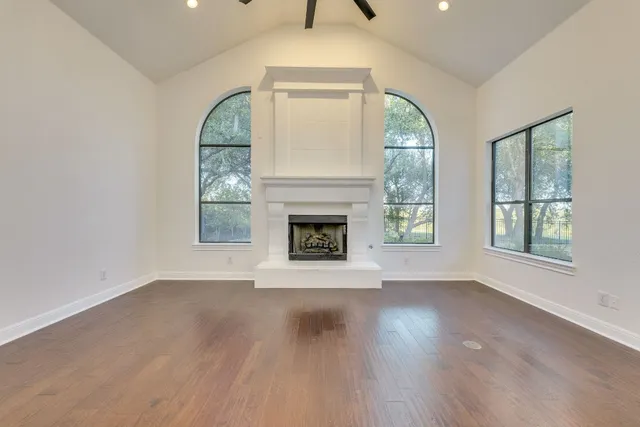 an empty room with wooden floor fireplace and windows