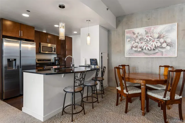 a kitchen with stainless steel appliances kitchen island granite countertop a dining table chairs and a refrigerator