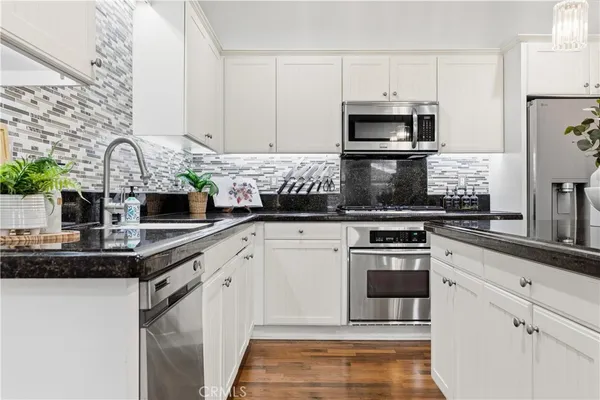 a kitchen with stainless steel appliances a refrigerator a sink dishwasher a stove and white cabinets with wooden floor
