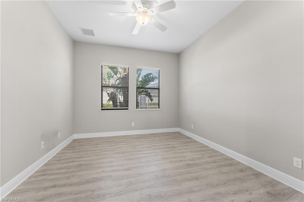 4711 Abaca Circle Naples, FL 34119 - Photo 12 of 32 an empty room with wooden floor chandelier fan and windows