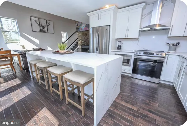 a kitchen with stainless steel appliances granite countertop a kitchen island a stove a refrigerator cabinets and a chairs