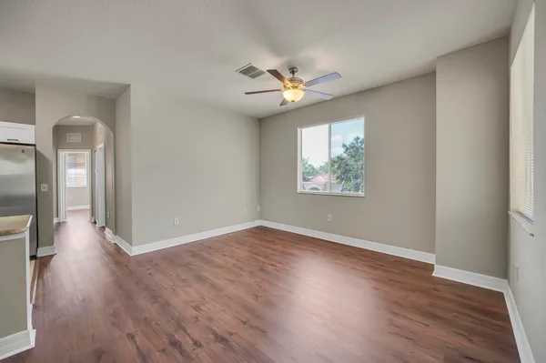 an empty room with wooden floor chandelier fan and windows