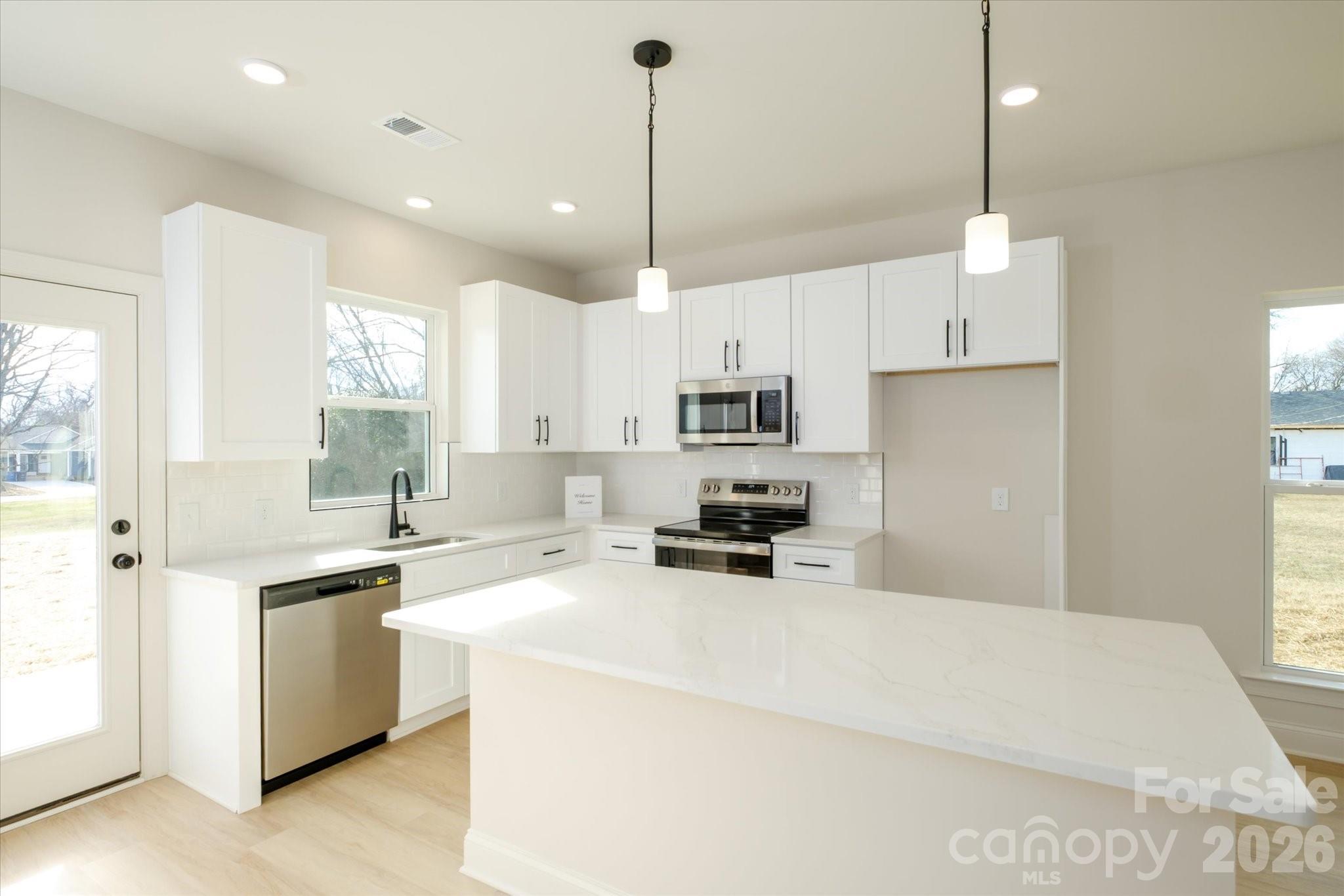1816 East Greenbriar Road Statesville, NC 28625 - Photo 5 of 34 a kitchen with kitchen island a sink a stove a refrigerator and white cabinets next to a window