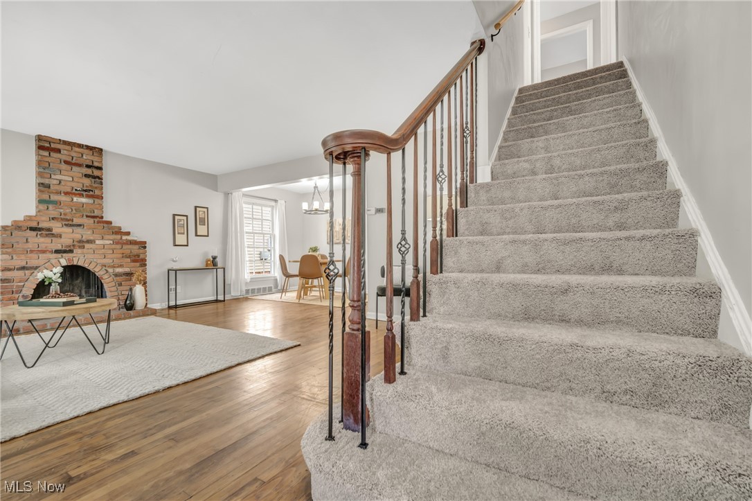 2440 White Road Cleveland, OH 44118 - Photo 17 of 43 Stairs featuring wood-type flooring, a fireplace, and a chandelier