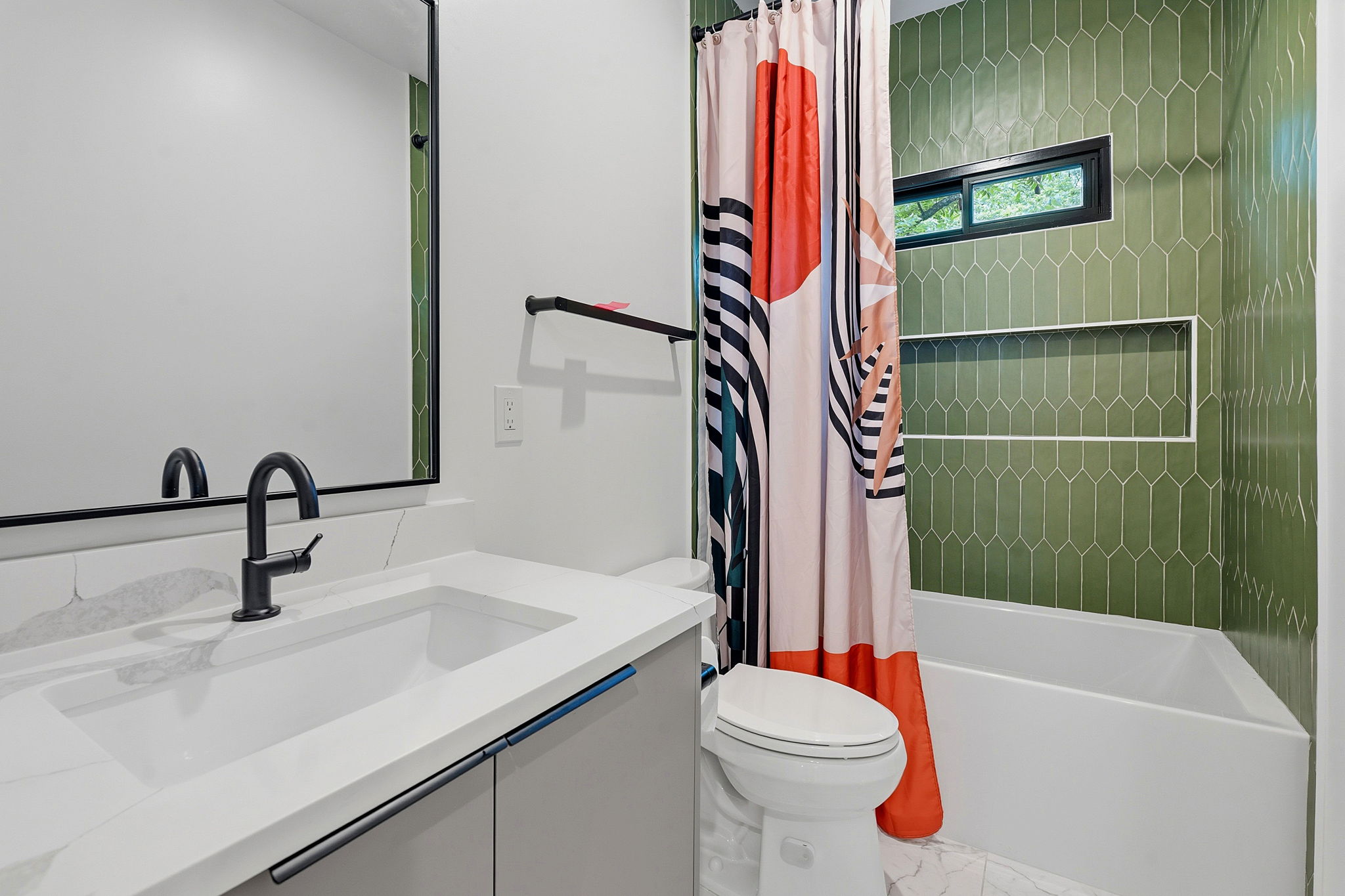 2004 Riverview Street Austin, TX 78702 - Photo 29 of 36 Bathroom featuring a contemporary vanity with a white countertop and integrated sink, a rectangular framed mirror, matte black fixtures, and a bathtub with green picket tile surround and a recessed niche