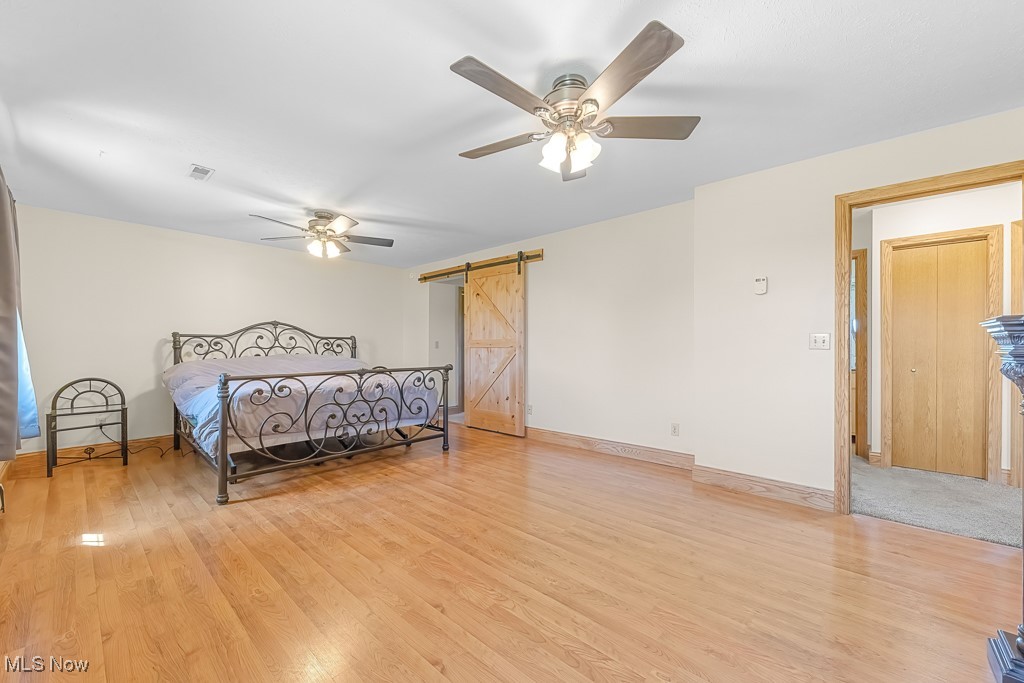 8690 Friendsville Road Lodi, OH 44254 - Photo 24 of 50 Bedroom featuring a barn door, light wood-style floors, ceiling fan, visible vents, and baseboards