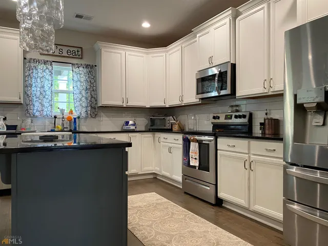 a kitchen with stainless steel appliances granite countertop white cabinets a sink a stove a microwave and a window