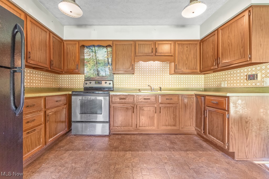 Kitchen with stainless steel electric stove, a textured ceiling, sink, and black fridge
