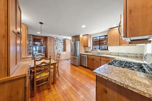 a kitchen with stainless steel appliances granite countertop a stove top oven a sink dishwasher a dining table and chairs with wooden floor