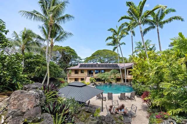 a front view of a house with a yard with plants and palm trees