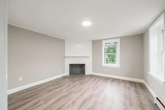 an empty room with wooden floor fireplace and windows