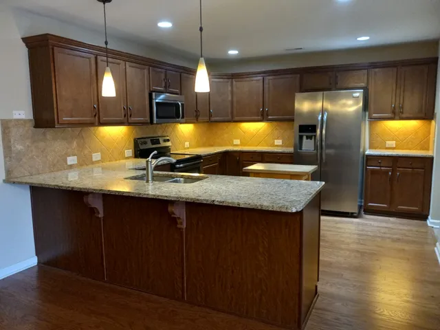 a kitchen with stainless steel appliances granite countertop wooden cabinets a refrigerator a sink a stove and wooden floors