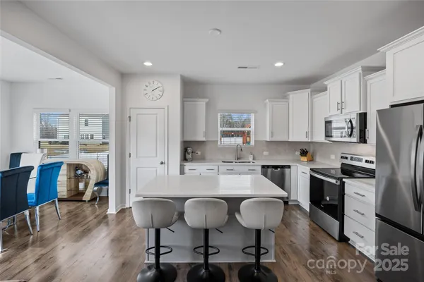 a kitchen with stainless steel appliances kitchen island granite countertop a refrigerator a stove a sink dishwasher and white cabinets with wooden floor
