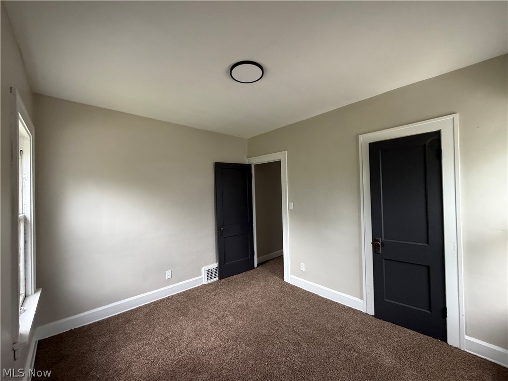 15317 Shiloh Road Cleveland, OH 44110 - Photo 23 of 29 Carpeted room featuring a window, two dark-paneled doors with white trim, a flush-mount ceiling light, and light-toned walls