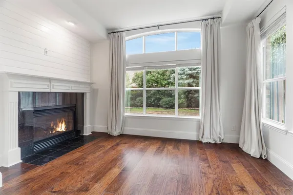 a view of an empty room with wooden floor fireplace and a window