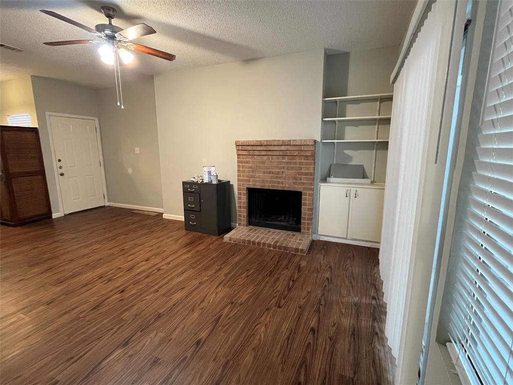 9502 Kempler Drive, Unit B Austin, TX 78748 - Photo 11 of 18 Unfurnished living room featuring dark wood finished floors, a ceiling fan, a fireplace, and a textured ceiling