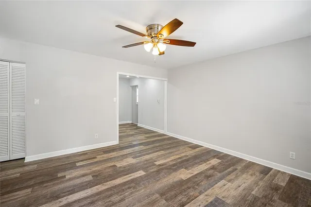 a view of an empty room with wooden floor and a ceiling fan