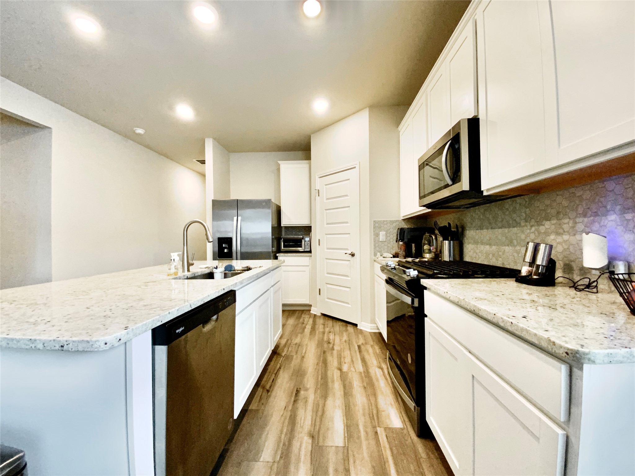 246 El Capitan Loop Dripping Springs, TX 78620 - Photo 12 of 37 Kitchen featuring stainless steel appliances, light wood finished floors, a kitchen island with sink, light stone countertops, and recessed lighting