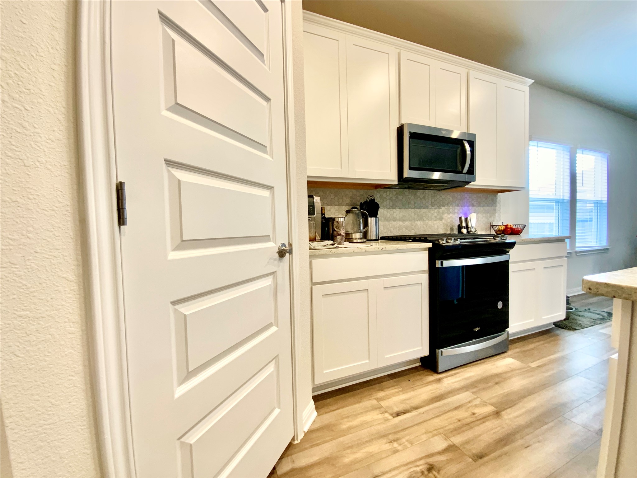 246 El Capitan Loop Dripping Springs, TX 78620 - Photo 13 of 37 Kitchen with stainless steel appliances, white cabinetry, light wood-style flooring, and tasteful backsplash