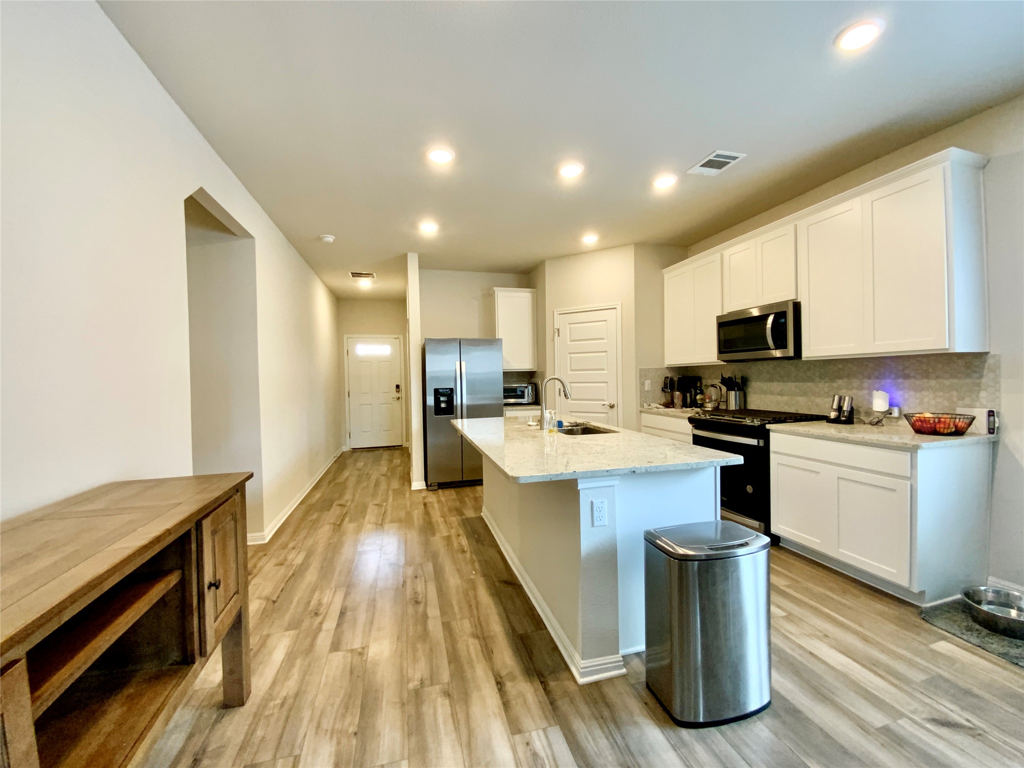 246 El Capitan Loop Dripping Springs, TX 78620 - Photo 10 of 37 Kitchen featuring stainless steel appliances, light stone countertops, a kitchen island with sink, white cabinets, and light wood-style floors