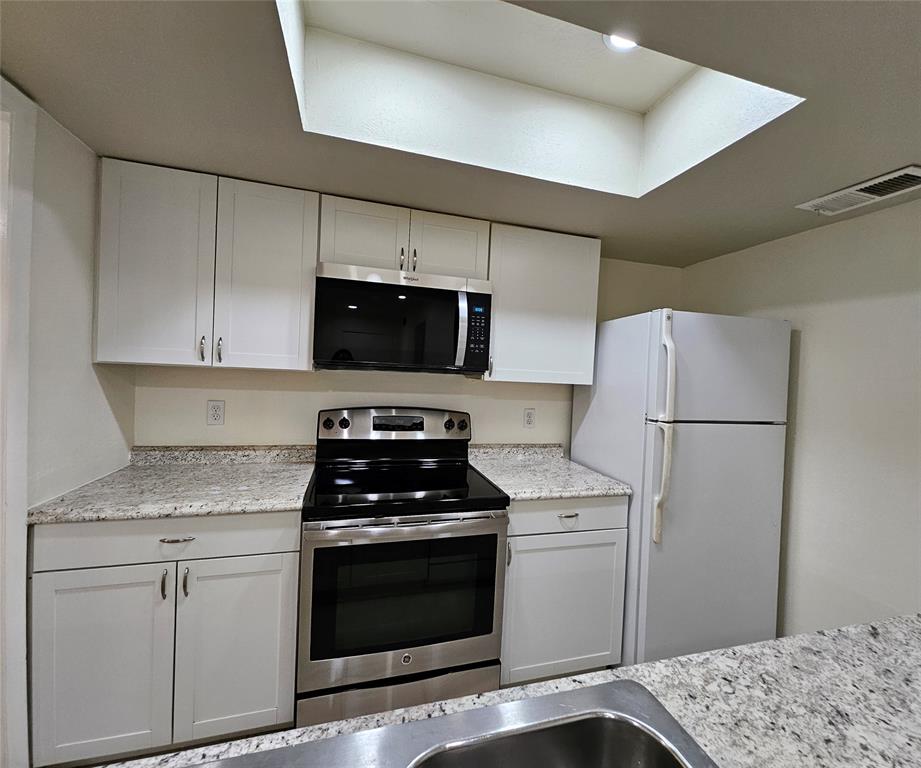 12816 Midway Road, Unit 1067 Dallas, TX 75244 - Photo 10 of 19 Modern kitchen featuring a skylight, white shaker-style cabinetry, a stainless steel electric range, a built-in microwave,