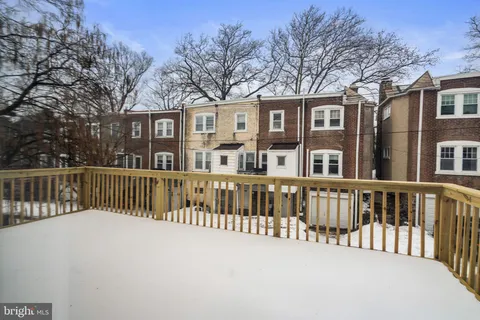 a view of a brick house with large wooden fence and large trees