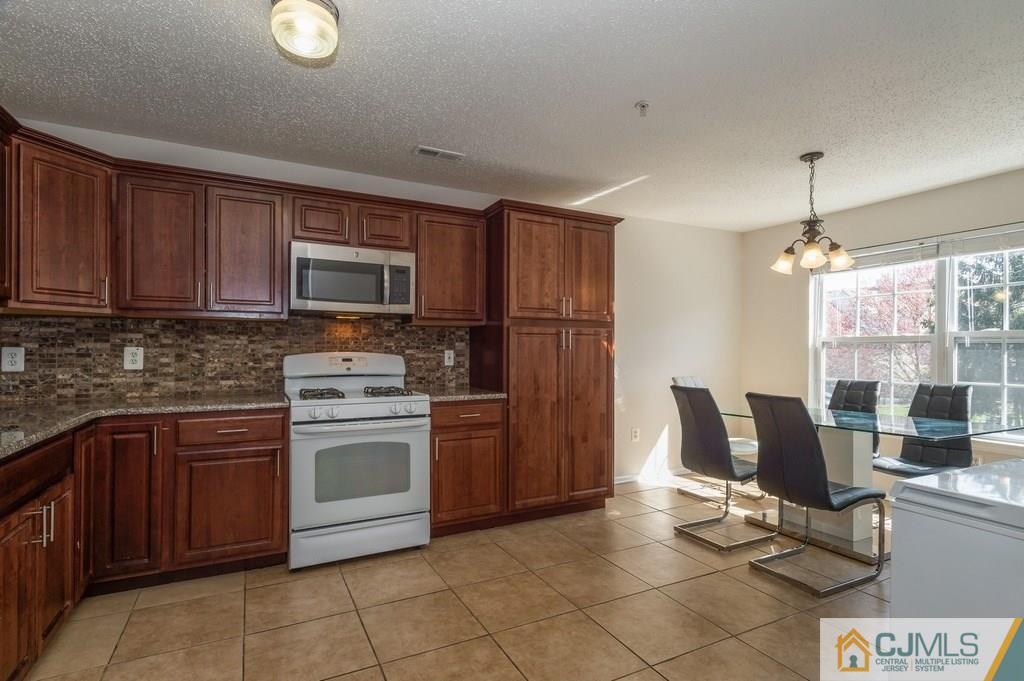 85 Prestwick Way, Unit 85 Edison, NJ 08820 - Photo 7 of 18 a kitchen with stainless steel appliances granite countertop a stove top oven a sink dishwasher a dining table and chairs with wooden floor