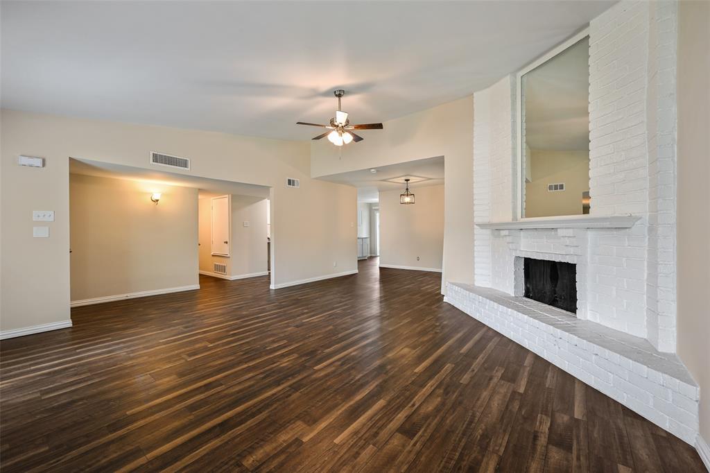 7318 Emory Oak Lane Dallas, TX 75249 - Photo 21 of 28 Spacious interior featuring wood-finish flooring, a white-painted brick fireplace with a mantel, vaulted ceilings, and a ceiling fan with integrated lighting