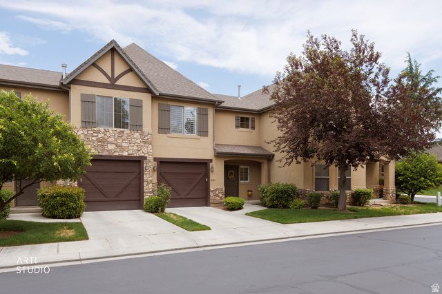 6761 950 East Midvale, UT 84047 - Photo 2 of 44 Stucco and stone facade featuring decorative gable accents, two single-car garage doors with carriage house styling, and mature landscaping