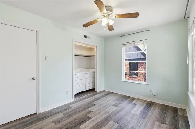 an empty room with wooden floor chandelier fan and windows