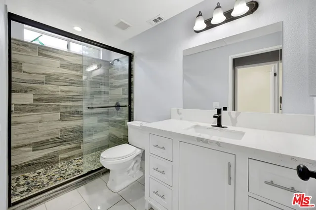 a bathroom with a granite countertop sink a toilet a mirror and shower