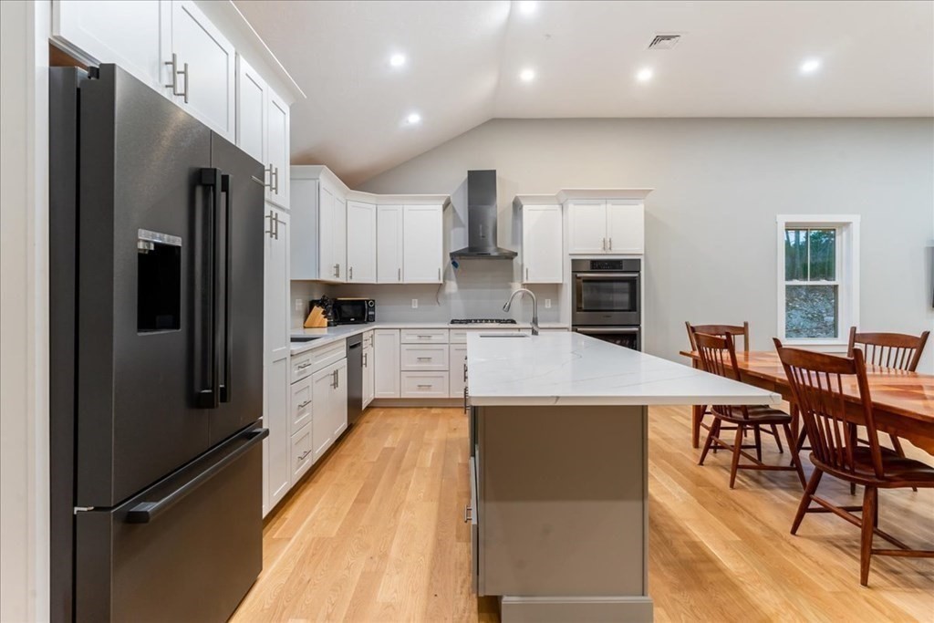 185 Kimball Road Amesbury, MA 01913 - Photo 10 of 24 a kitchen with stainless steel appliances kitchen island granite countertop a refrigerator a stove a sink a dining table and chairs with wooden floor