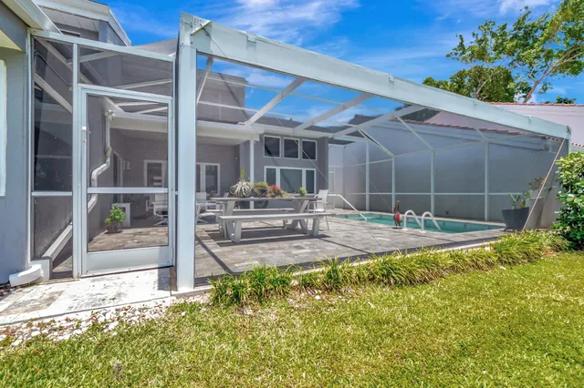 a view of a swimming pool with lawn chairs plants and large tree