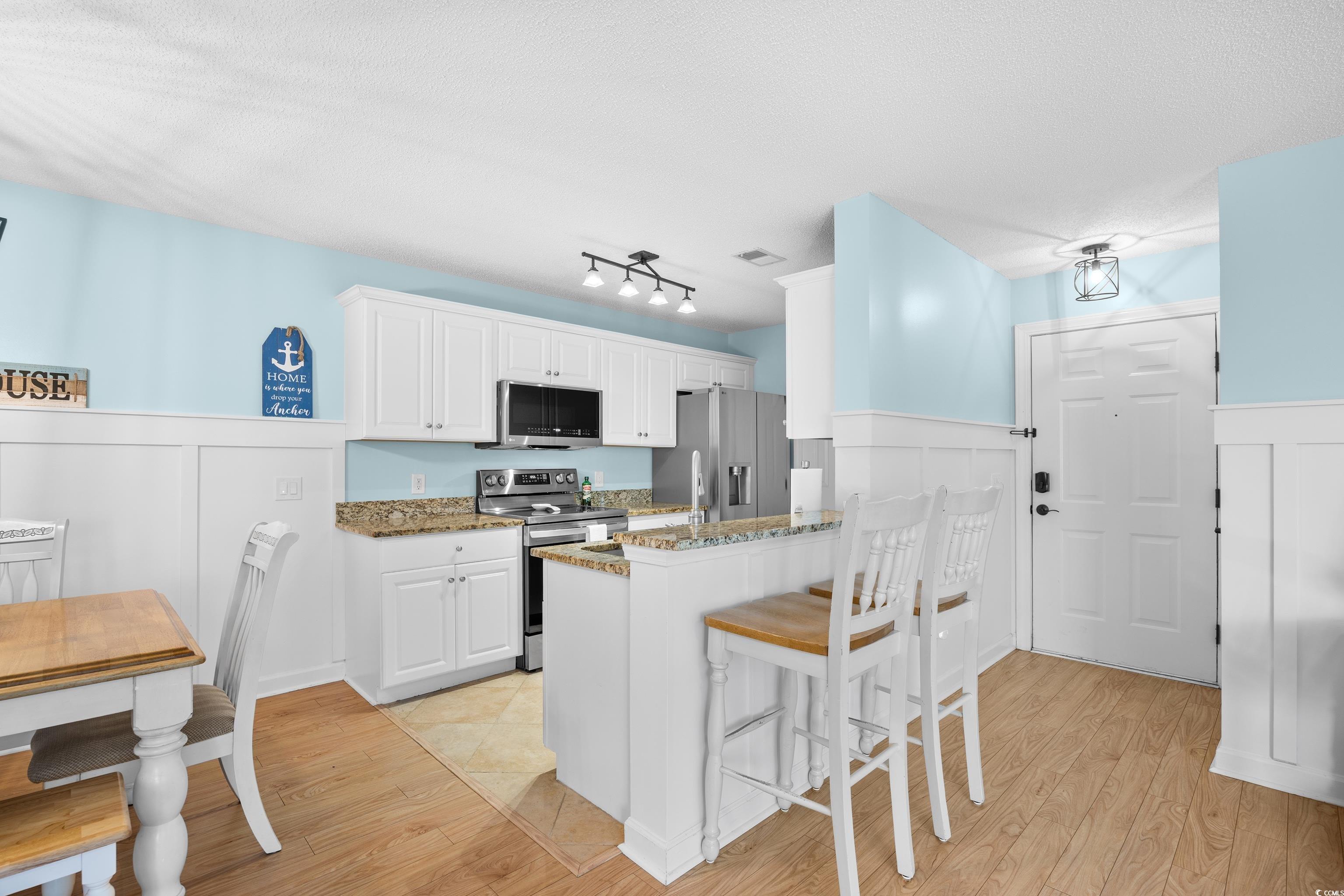 4277 Santolina Way, Unit D Murrells Inlet, SC 29576 - Photo 11 of 40 Kitchen with light wood-style floors, a kitchen breakfast bar, white cabinets, light stone countertops, and stainless steel appliances