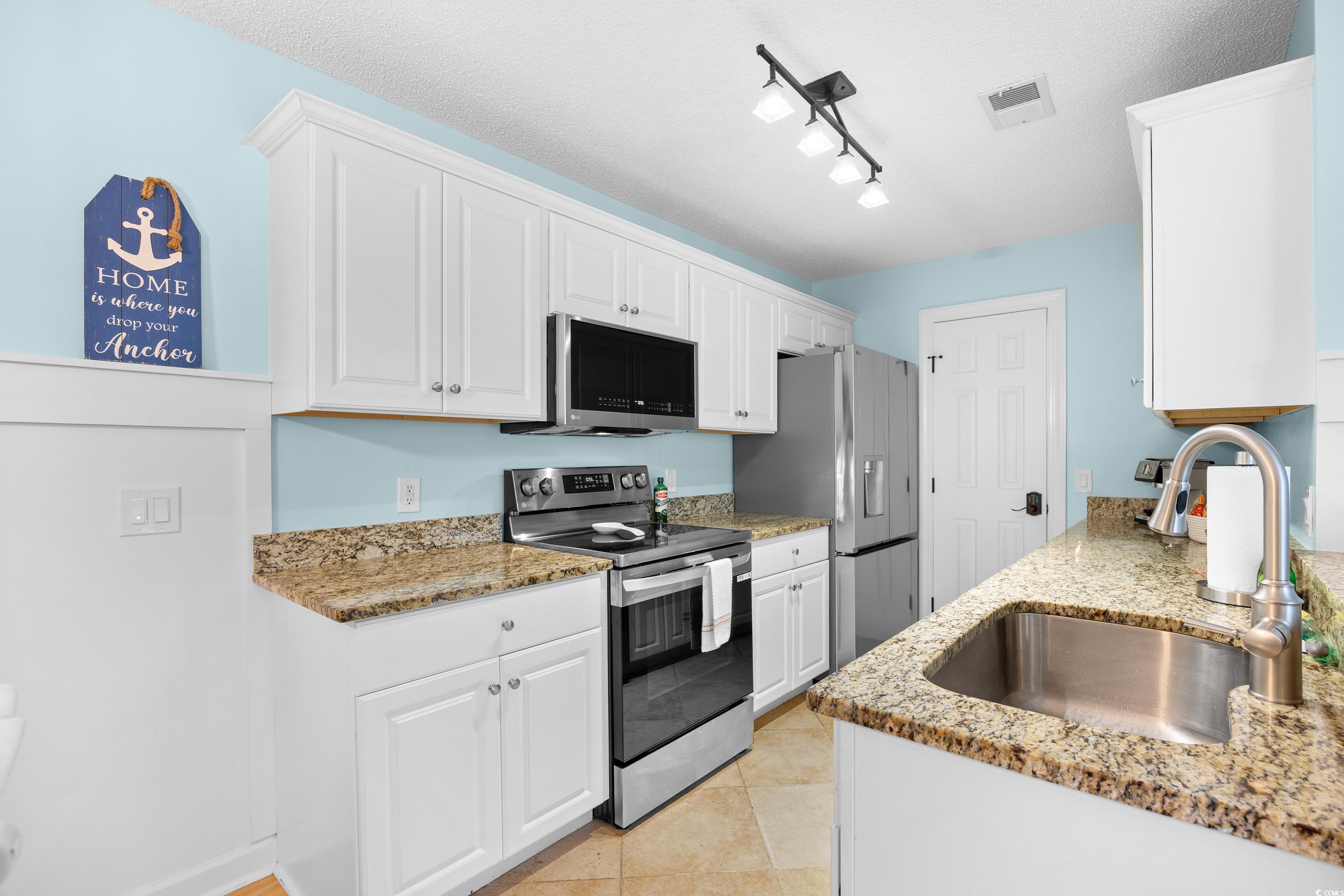 4277 Santolina Way, Unit D Murrells Inlet, SC 29576 - Photo 12 of 40 Kitchen with appliances with stainless steel finishes, light stone counters, white cabinetry, light tile patterned flooring, and a textured ceiling