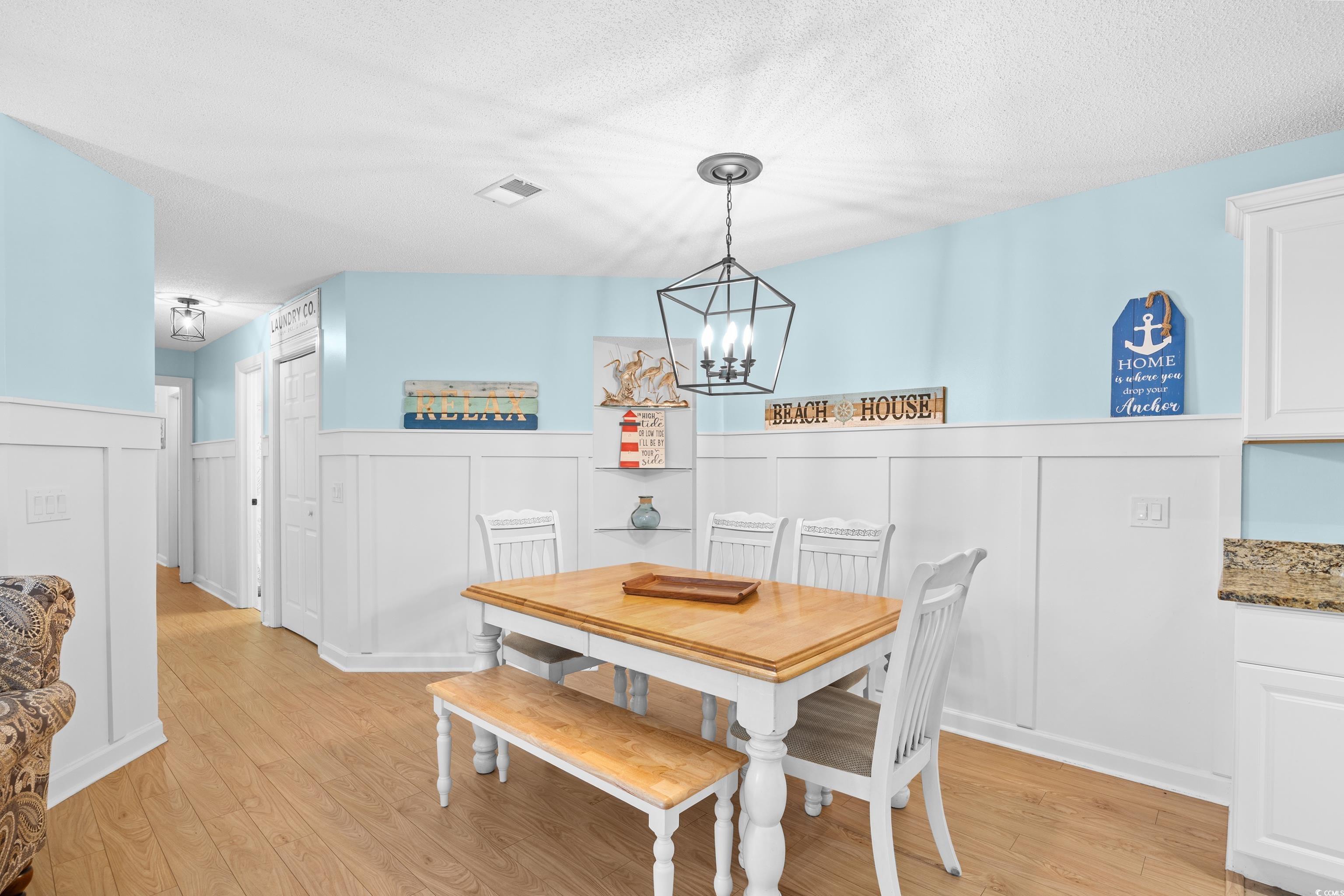 4277 Santolina Way, Unit D Murrells Inlet, SC 29576 - Photo 9 of 40 Dining space with light wood finished floors, a textured ceiling, a wainscoted wall, a chandelier, and a decorative wall