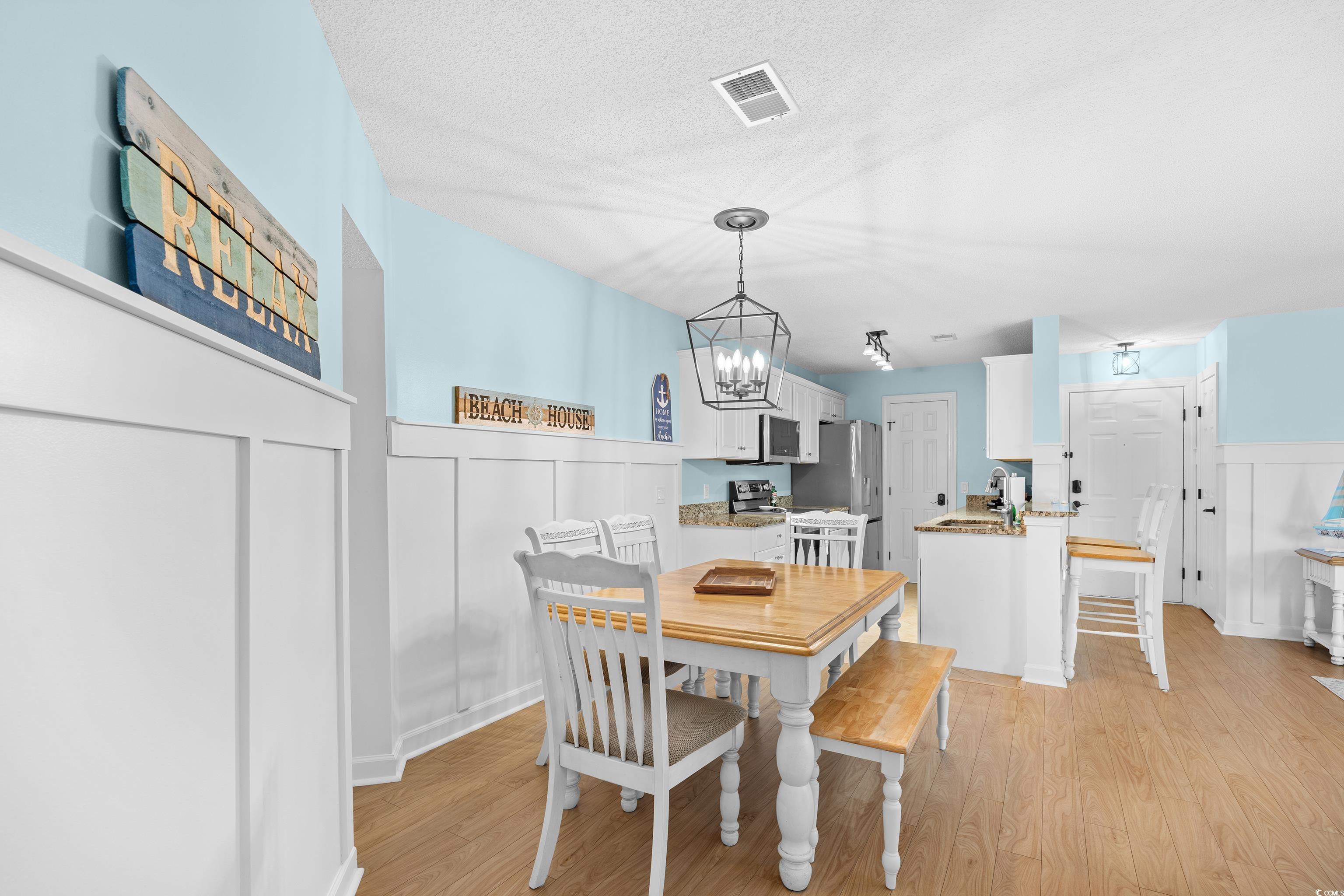 4277 Santolina Way, Unit D Murrells Inlet, SC 29576 - Photo 10 of 40 Dining area featuring a decorative wall, wainscoting, a chandelier, a textured ceiling, and light wood-type flooring