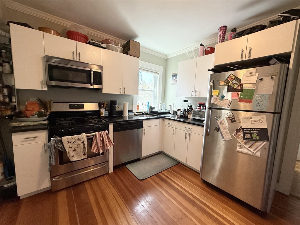 a white kitchen with stainless steel appliances granite countertop a stove a sink and a microwave