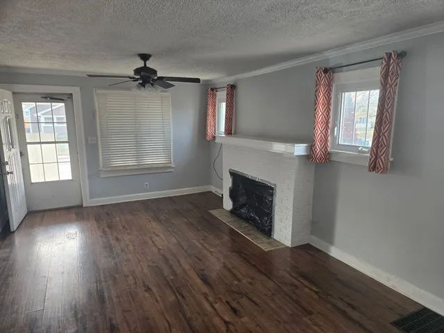 an empty room with wooden floor fireplace and windows