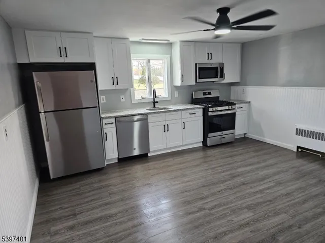 a kitchen with granite countertop a refrigerator a sink a stove a microwave and wooden floors