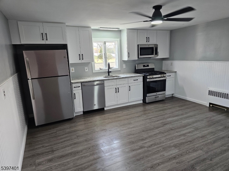 a kitchen with granite countertop a refrigerator a sink a stove a microwave and wooden floors