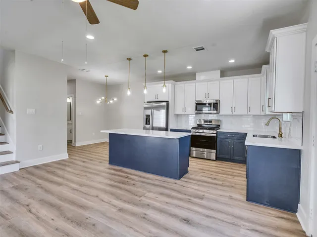 a large kitchen with stainless steel appliances granite countertop a large kitchen island a sink dishwasher a refrigerator and white countertops with wooden floor